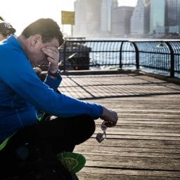 Man sitting on a pier rubbing his eyes out of exhaustion