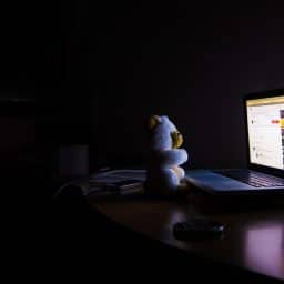 Teddy bear in darkened room facing computer screen